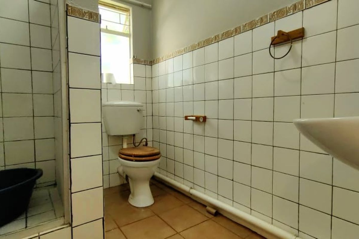 A dated bathroom featuring a shower enclosure, pedestal basin, and toilet with white wall tiling and exposed plumbing.