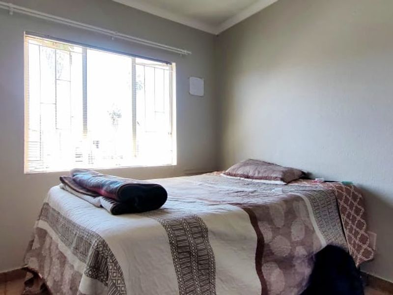 A standard bedroom featuring tiled flooring, neutral wall tones, and a window fitted with security bars.