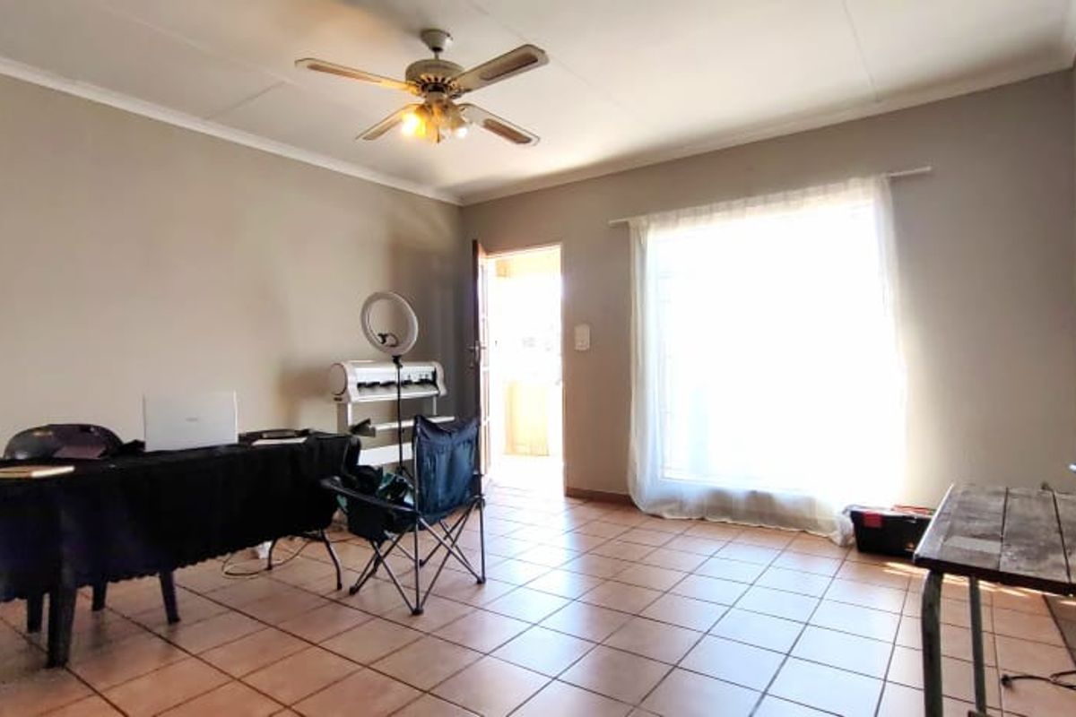 A living room area featuring tiled flooring, a ceiling fan, and a sliding glass door providing access to the exterior.
