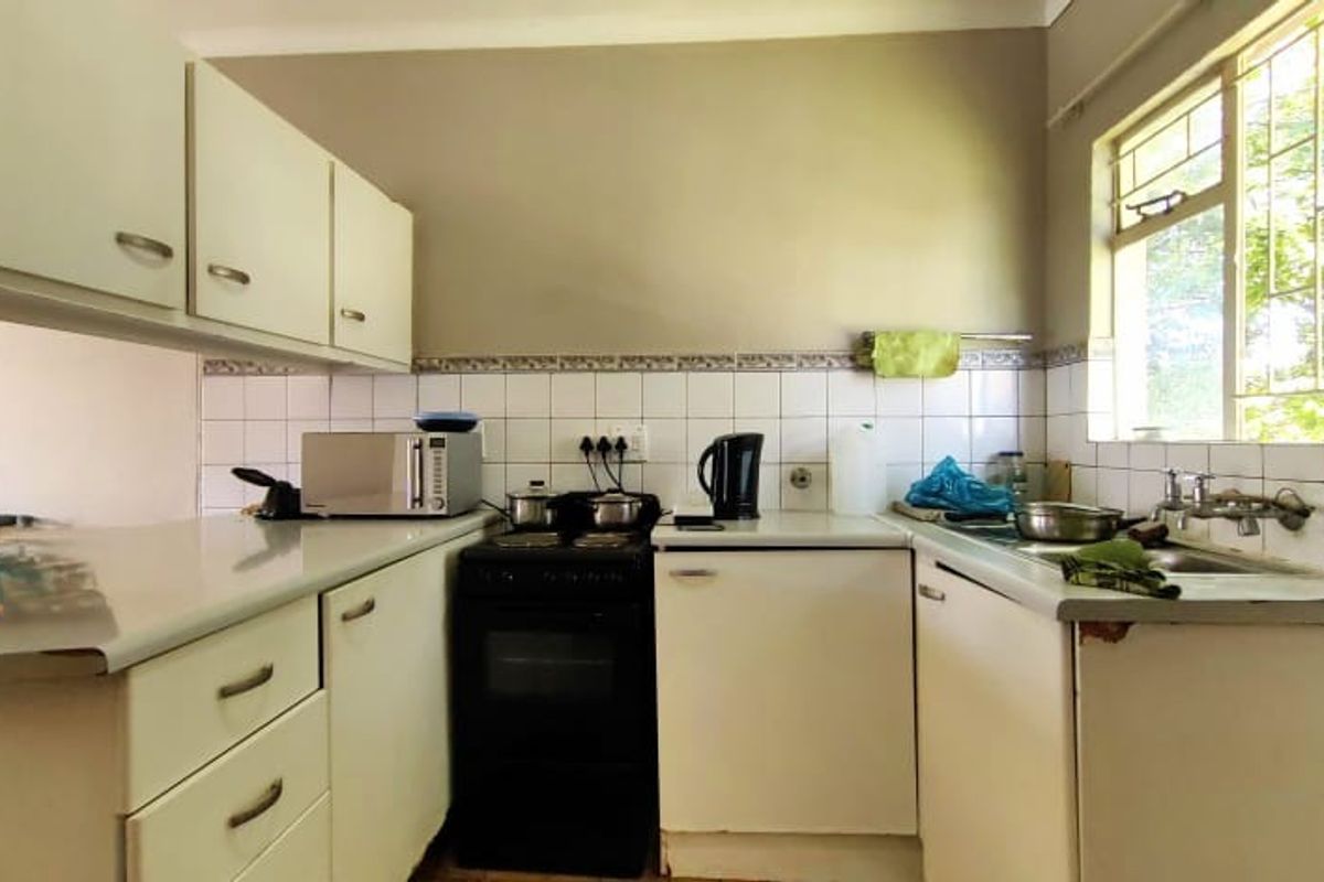 A compact kitchen featuring white cabinetry, tiled backsplash, a freestanding stove, and a stainless steel sink with a window view.