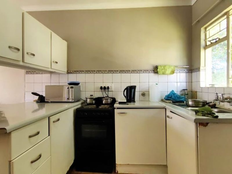 A compact kitchen featuring white cabinetry, tiled backsplash, a freestanding stove, and a stainless steel sink with a window view.