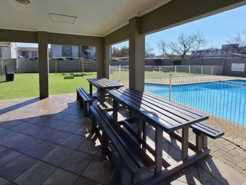 A covered outdoor patio area overlooking a communal swimming pool and landscaped garden space within the apartment complex.
