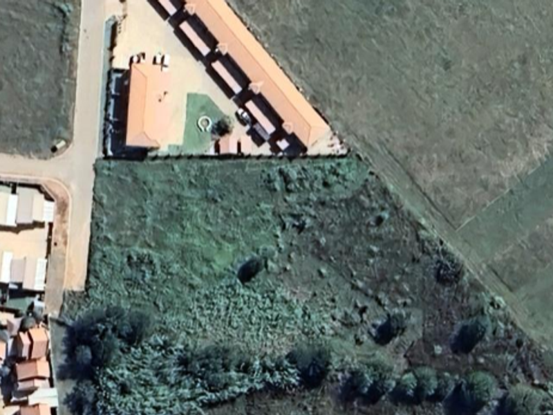 An aerial view of a vacant residential plot situated adjacent to an existing housing development.