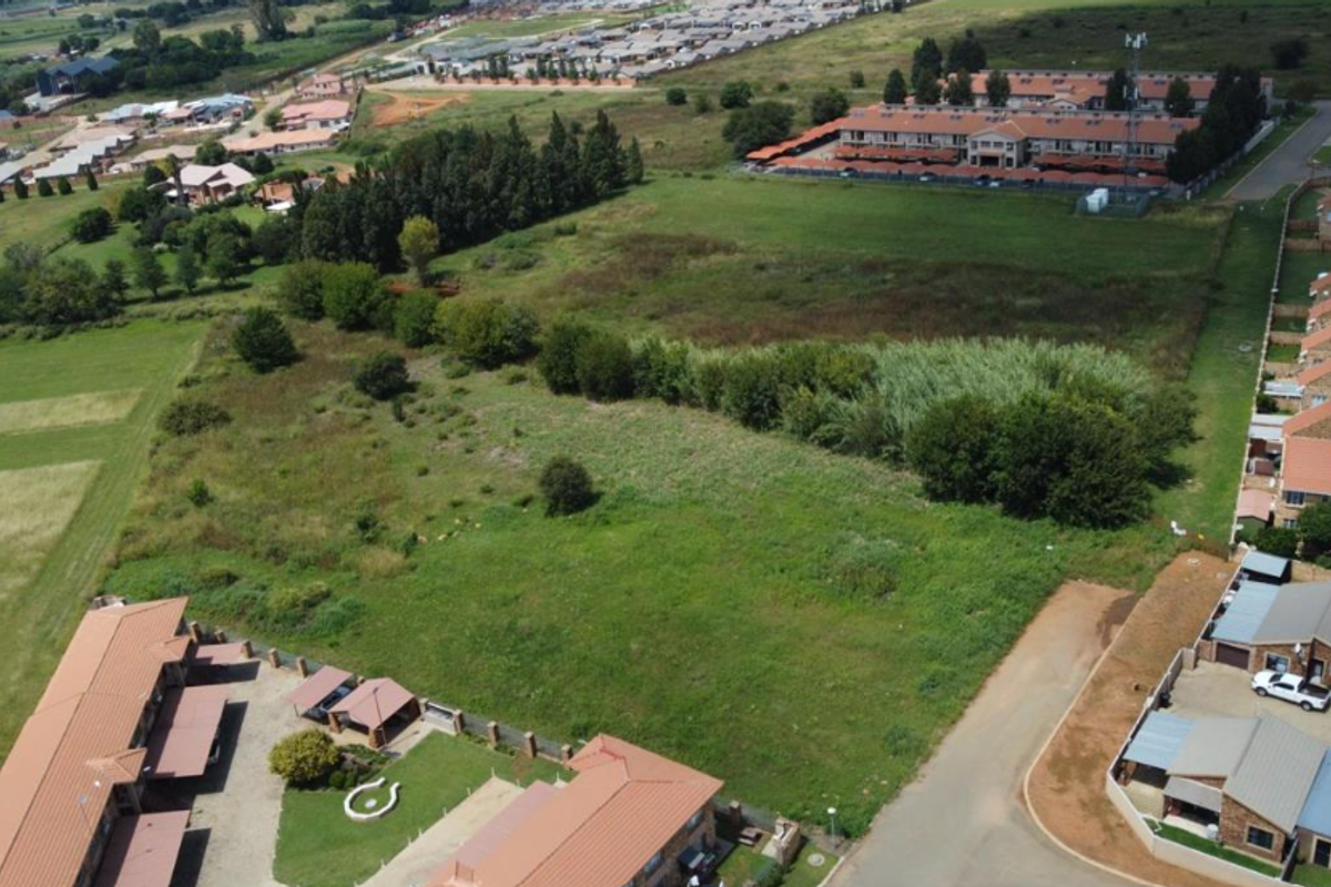 Aerial view of a vacant residential plot situated within an established suburban neighborhood, showing surrounding housing developments and access roads.