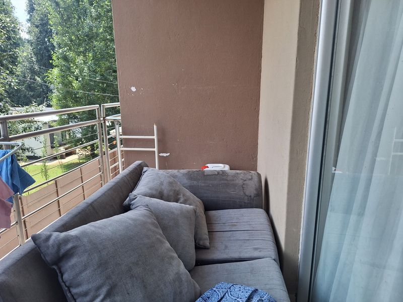 A compact balcony featuring a stainless steel railing and sliding glass door access, with visible wear on the exterior wall finish.