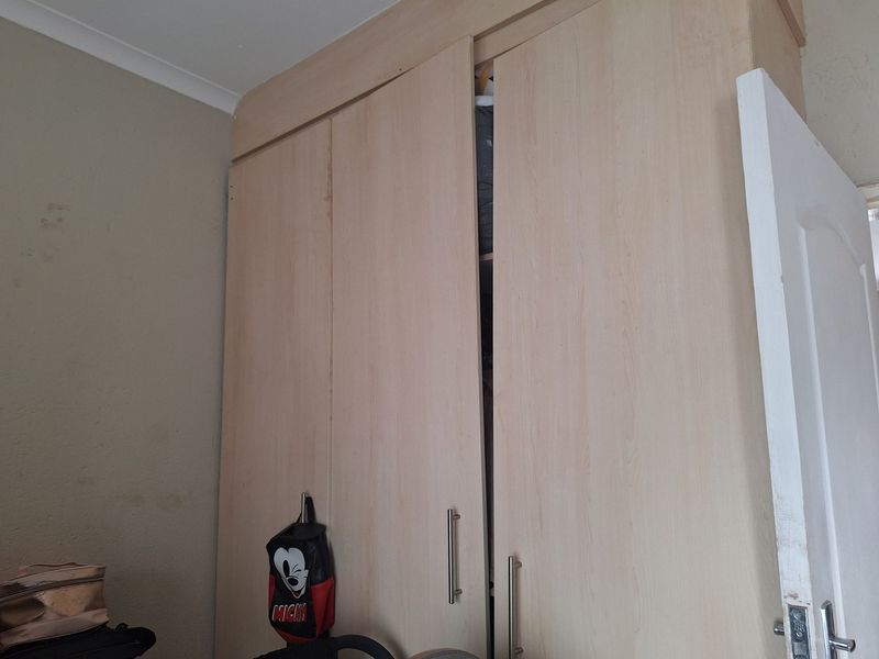 A bedroom featuring light wood-finish built-in wardrobes with modern handles and ceiling coving.