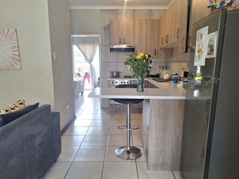Open-plan kitchen featuring wood-look cabinetry, a breakfast counter, and tiled flooring, seamlessly connecting to the living area and adjacent room.