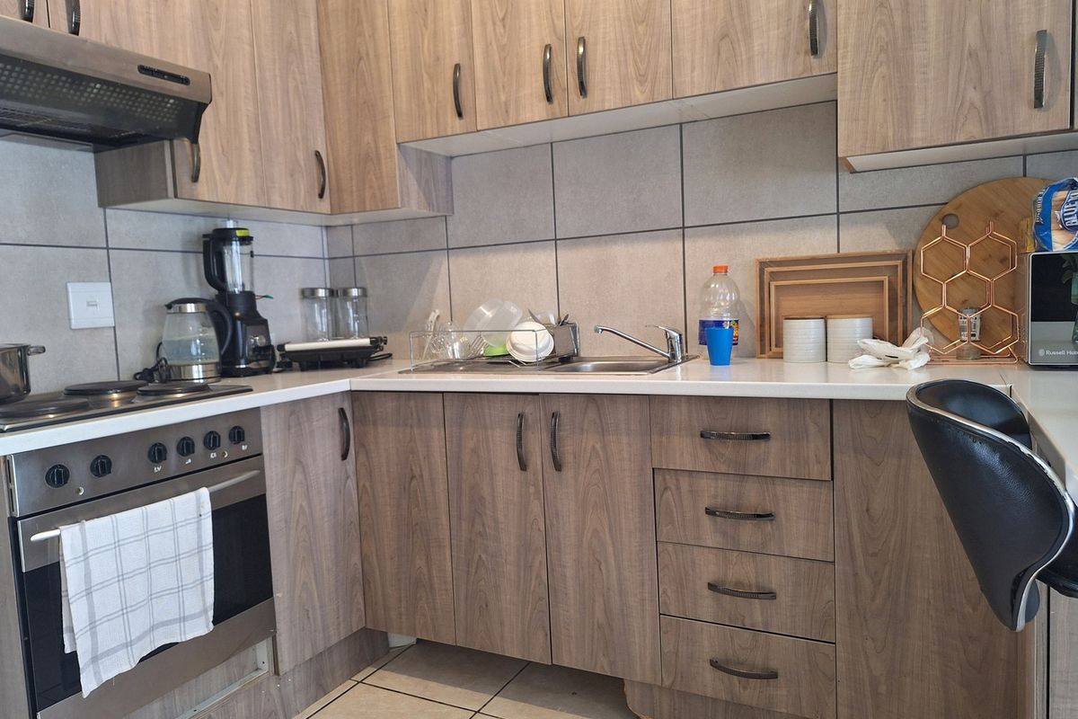 A functional kitchen featuring wood-look laminate cabinetry, built-in oven with hob, tiled backsplash, and a stainless steel sink.
