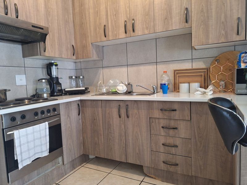 A functional kitchen featuring wood-look laminate cabinetry, built-in oven with hob, tiled backsplash, and a stainless steel sink.
