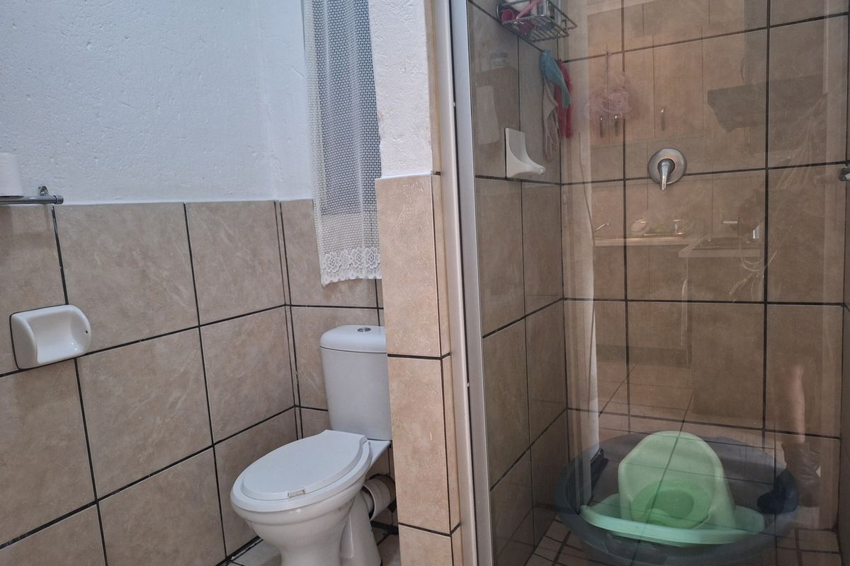 A functional bathroom featuring a toilet and a glass-enclosed shower with tiled walls and flooring.