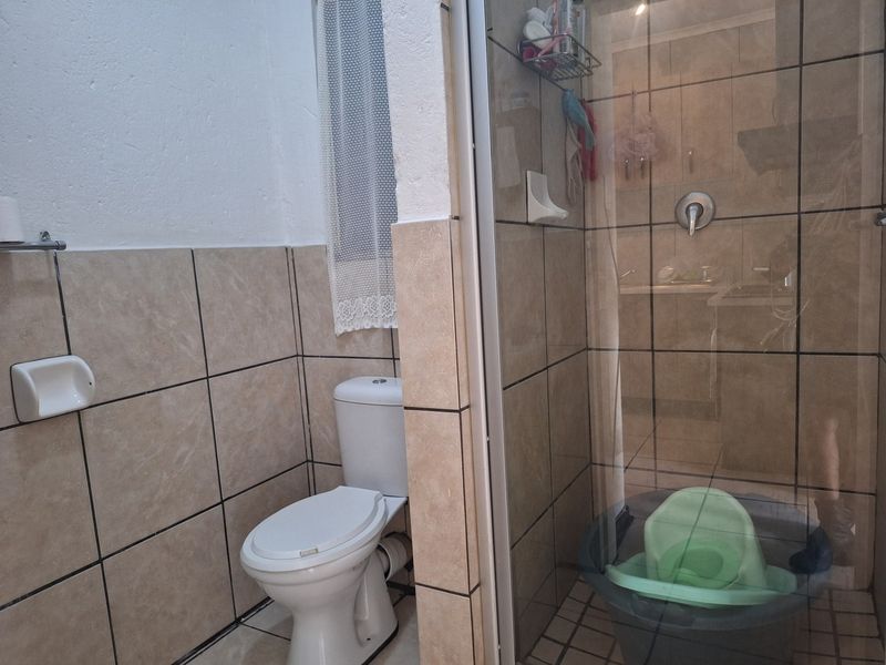 A functional bathroom featuring a toilet and a glass-enclosed shower with tiled walls and flooring.