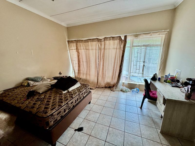 A bedroom featuring tiled flooring and a large sliding glass door with security gate, providing access to the exterior.