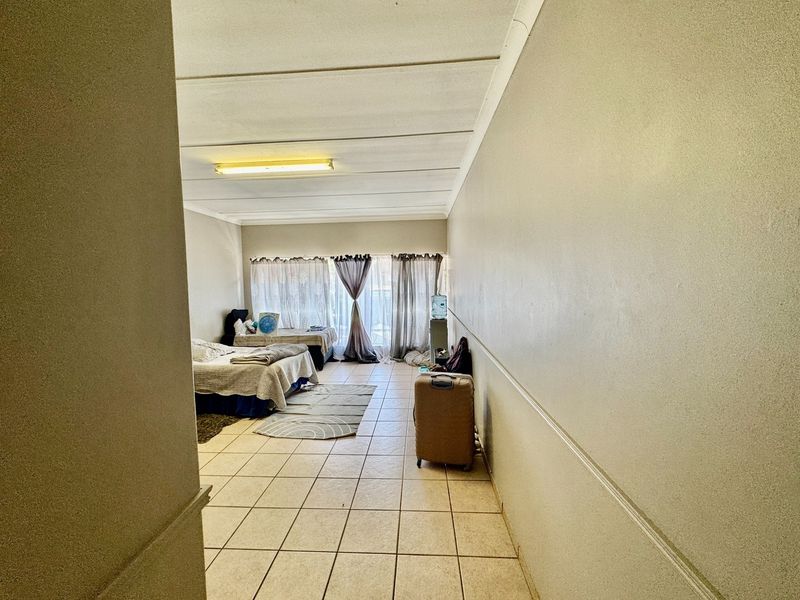 A spacious bedroom featuring tiled flooring and large windows with curtain rails, offering a blank canvas for potential renovation and interior design updates.