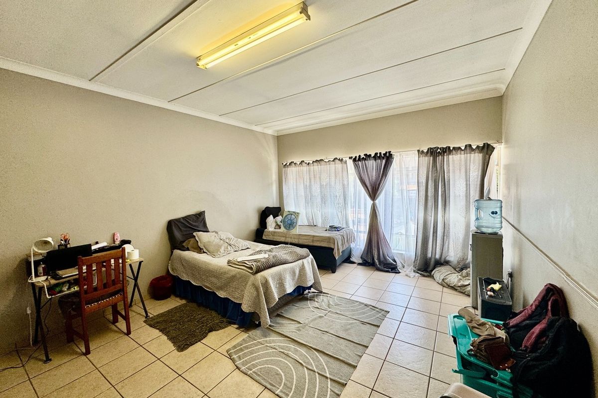 A bedroom featuring tiled flooring and a large window with curtain tracks, requiring minor ceiling repairs and cosmetic updates.