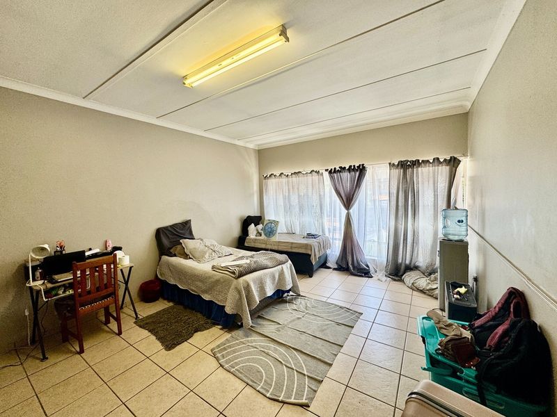 A bedroom featuring tiled flooring and a large window with curtain tracks, requiring minor ceiling repairs and cosmetic updates.