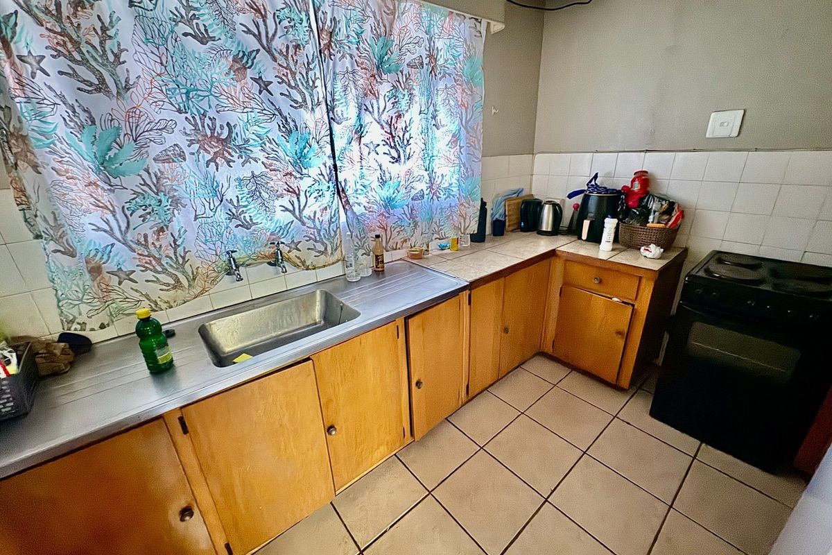 A dated kitchen featuring wooden cabinetry, a stainless steel sink, tiled splashback, and tiled flooring, requiring modernization to improve functionality and aesthetic appeal.