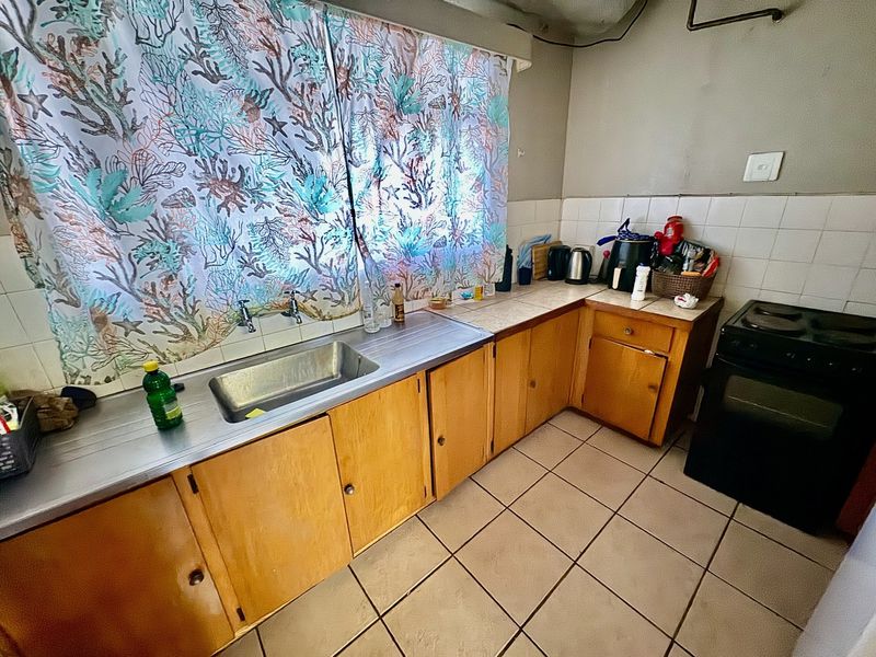 A dated kitchen featuring wooden cabinetry, a stainless steel sink, tiled splashback, and tiled flooring, requiring modernization to improve functionality and aesthetic appeal.