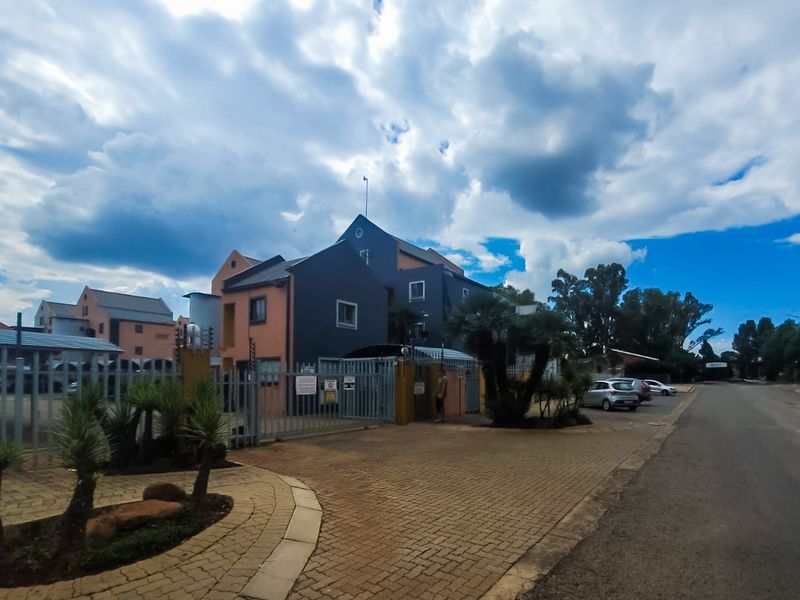Front exterior view of the apartment complex featuring paved driveway access, secure metal fencing, and multi-story residential buildings.