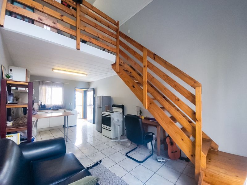 Open-plan living area featuring a wooden staircase leading to a mezzanine level, tiled flooring, and a functional kitchen space.