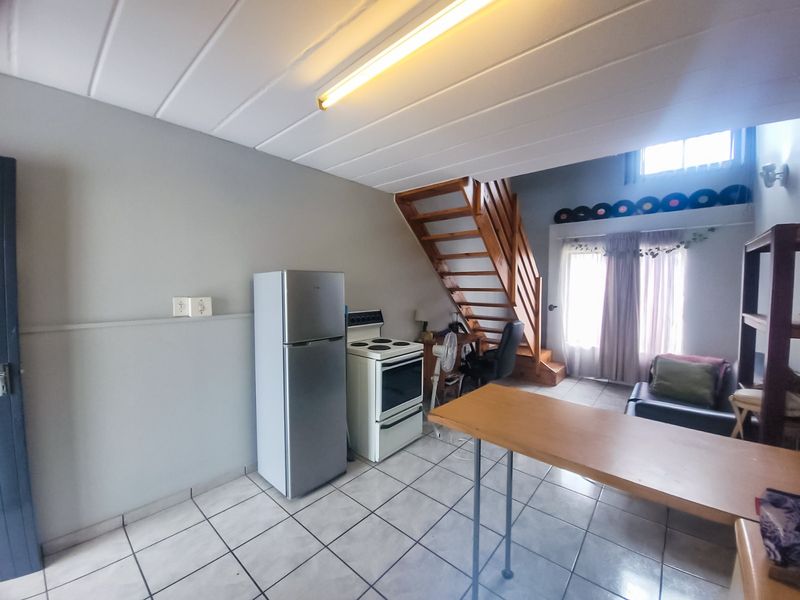 Open-plan living area featuring tiled floors, a wooden staircase, and a functional kitchen space with a freestanding stove.
