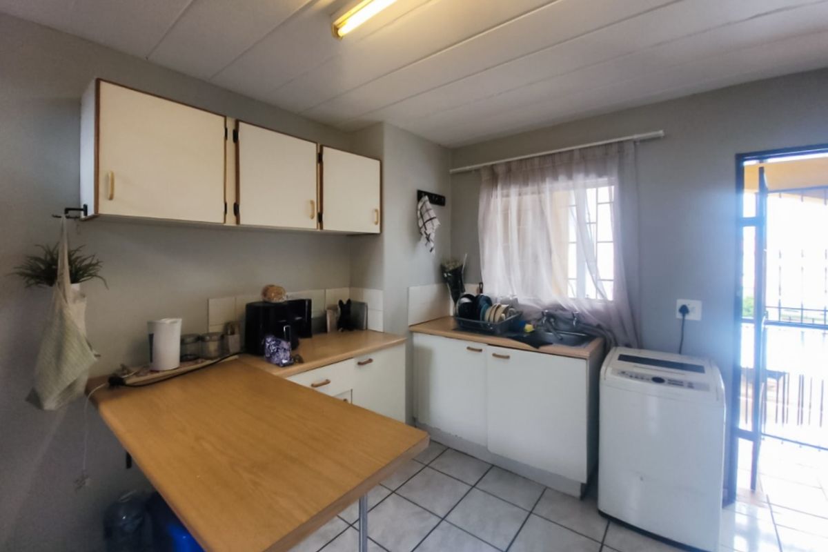 A functional kitchen featuring built-in cabinetry, laminate countertops, a stainless steel sink, and tiled flooring with direct access to an outdoor area.