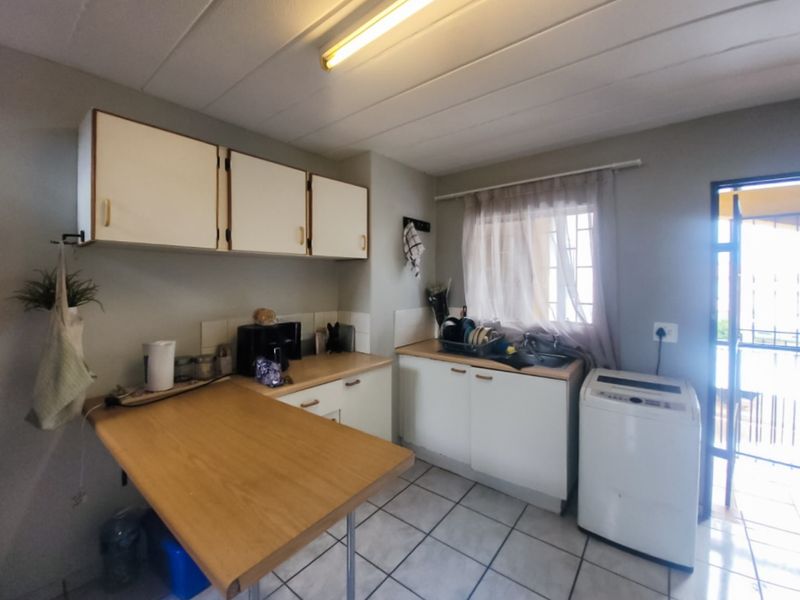 A functional kitchen featuring built-in cabinetry, laminate countertops, a stainless steel sink, and tiled flooring with direct access to an outdoor area.