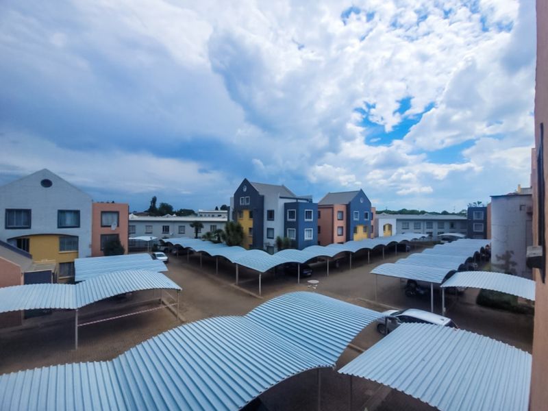An elevated view of an apartment complex courtyard featuring extensive covered parking bays and multi-story residential buildings under a cloudy sky.