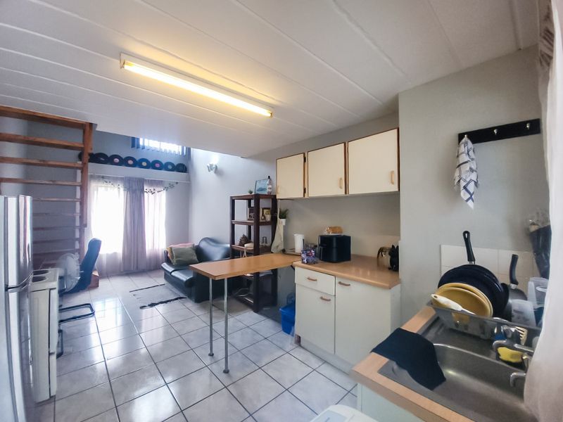 Open-plan living area featuring a functional kitchen with built-in cabinetry, laminate countertops, and tiled flooring, with an integrated staircase leading to an upper level.