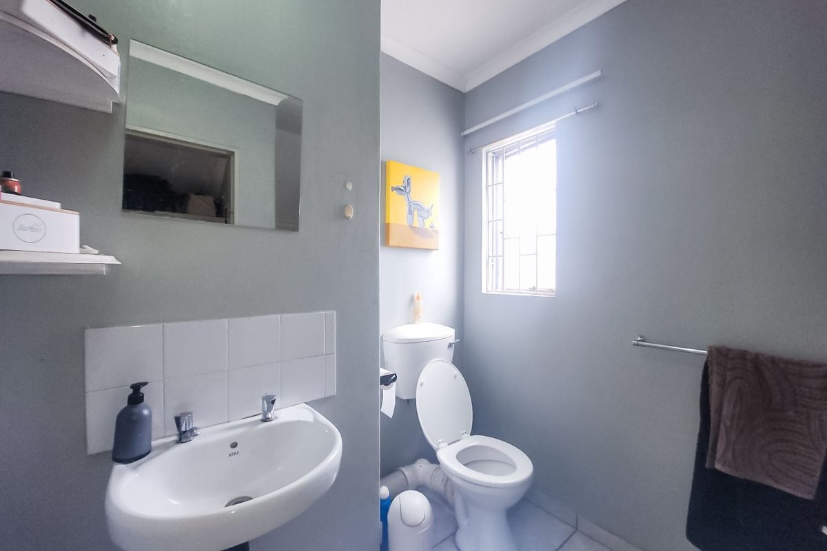 A functional bathroom featuring a ceramic basin with tiled splashback, a standard toilet, and a window with security bars.