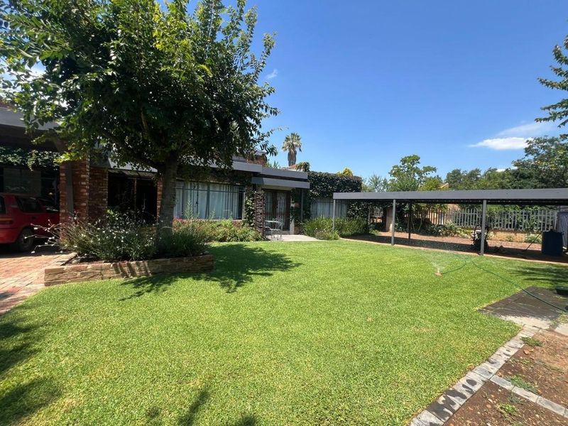 A well-maintained rear garden featuring a lush lawn, brick facade, and a functional carport structure.
