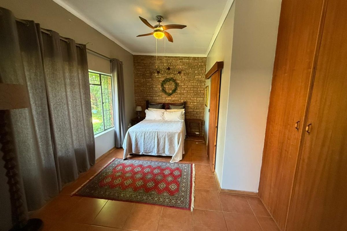 A bedroom featuring an exposed brick accent wall, tiled flooring, built-in wooden cupboards, and a ceiling fan.