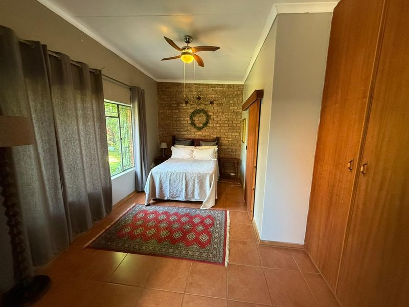 A bedroom featuring an exposed brick accent wall, tiled flooring, built-in wooden cupboards, and a ceiling fan.