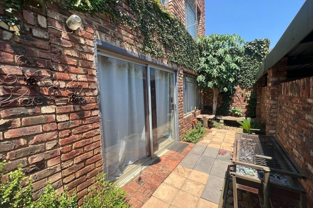 A private rear courtyard featuring exposed brick walls, paved flooring, and sliding glass door access to the main dwelling.
