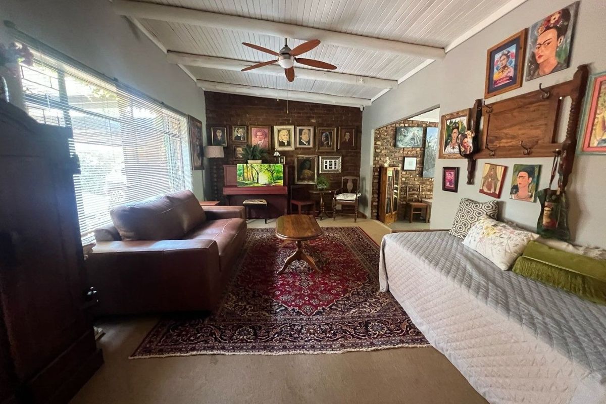 A spacious living room featuring an exposed brick feature wall, white painted exposed beam ceiling, and large windows providing ample natural light.