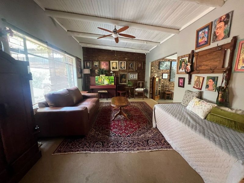 A spacious living room featuring an exposed brick feature wall, white painted exposed beam ceiling, and large windows providing ample natural light.