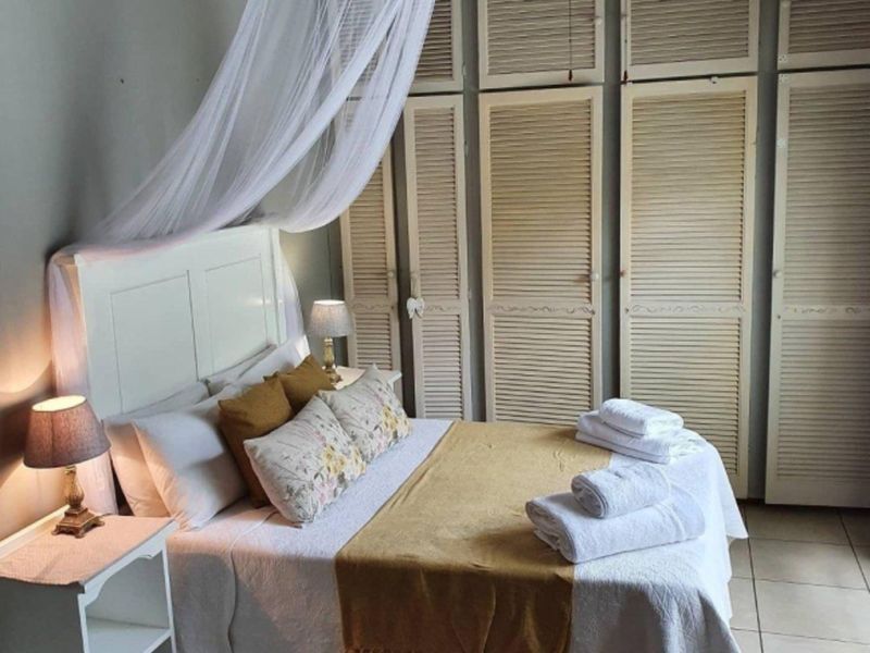 A cozy bedroom featuring built-in louvered cupboards and tiled flooring, offering a functional and well-maintained living space.