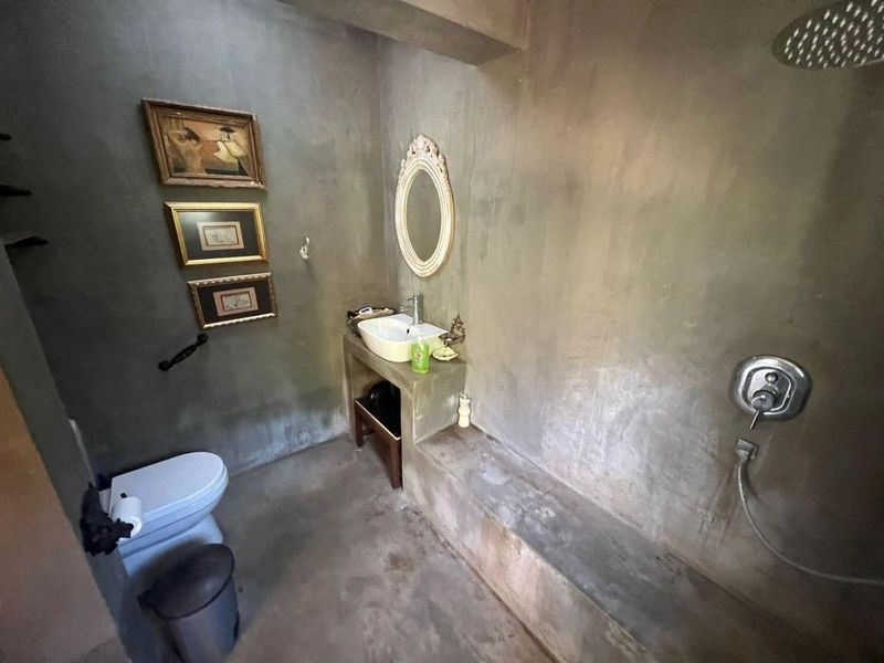 A rustic-style bathroom featuring a concrete vanity, vessel sink, and a walk-in shower area with a rain shower head and exposed concrete walls.