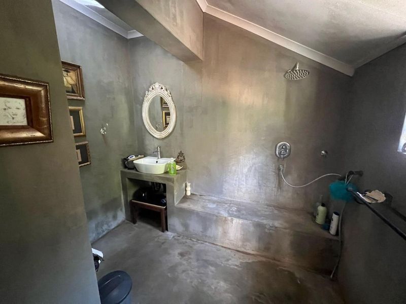A bathroom featuring industrial-style exposed concrete walls, a built-in concrete vanity with a vessel sink, and a walk-in shower area with a built-in bench.