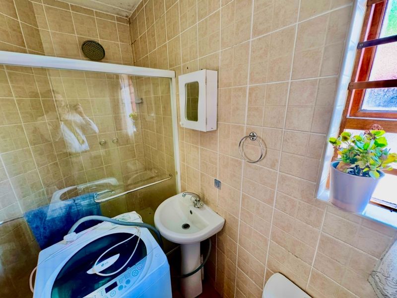 A compact bathroom featuring a pedestal sink, shower enclosure with glass door, and tiled walls. The space requires cosmetic updates to modernize the finishes.