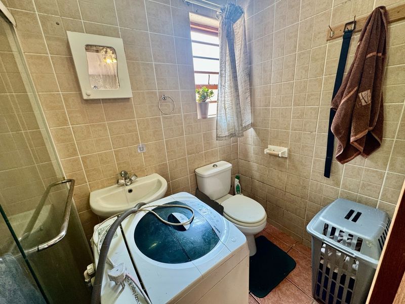 Compact bathroom featuring a shower enclosure, wall-mounted basin, and toilet, finished with floor-to-ceiling wall tiles.