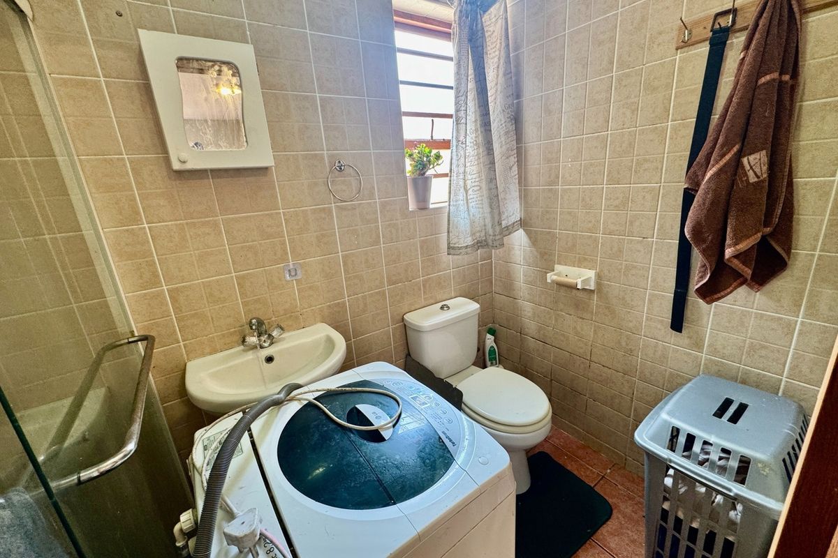 Compact bathroom featuring a shower enclosure, wall-mounted basin, and toilet, finished with floor-to-ceiling wall tiles.