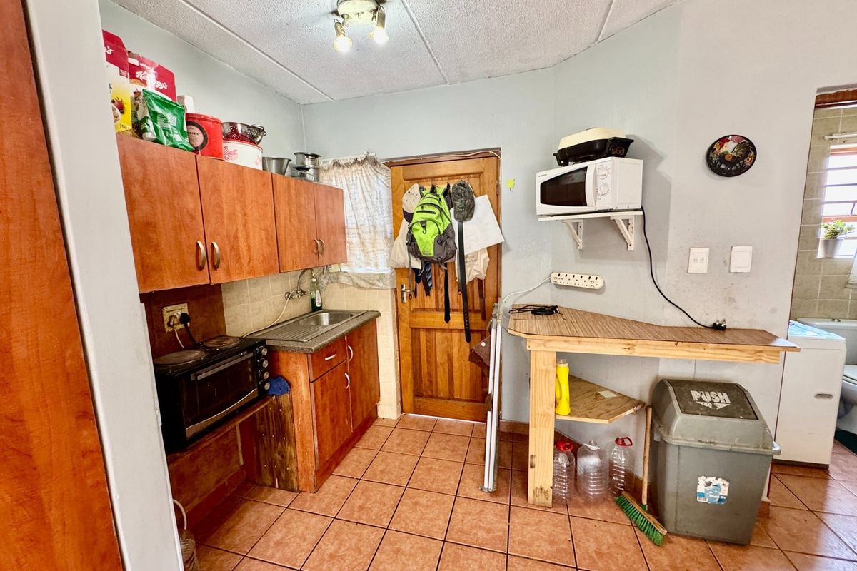 A compact kitchen area featuring wooden cabinetry, a stainless steel sink, and tiled flooring, offering potential for modernization and improved layout efficiency.