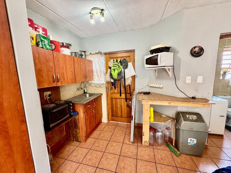 A compact kitchen area featuring wooden cabinetry, a stainless steel sink, and tiled flooring, offering potential for modernization and improved layout efficiency.