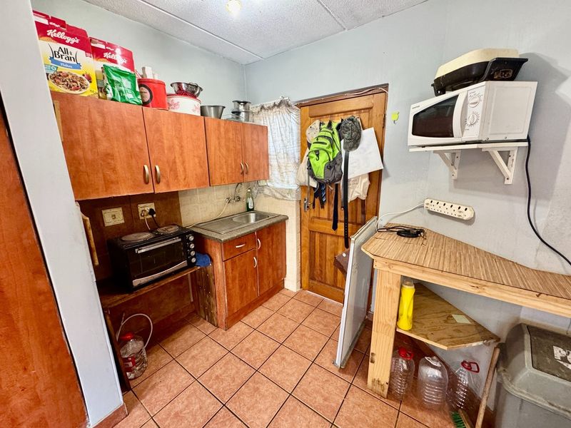 A compact scullery or utility area featuring laminate cabinetry, a stainless steel sink, and tiled flooring, offering functional prep space for the apartment.