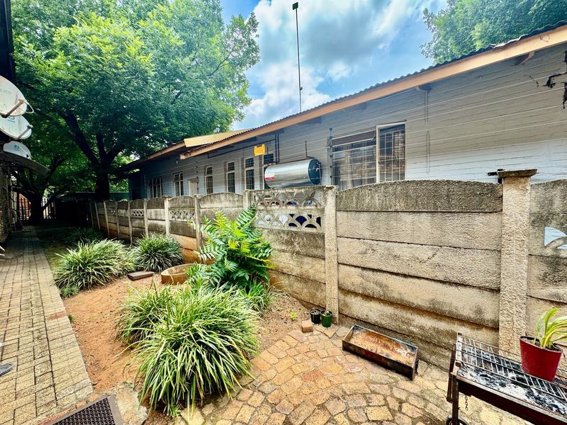 Rear exterior view of the property featuring a paved walkway, landscaped garden area, and a precast concrete boundary wall with an installed solar geyser.
