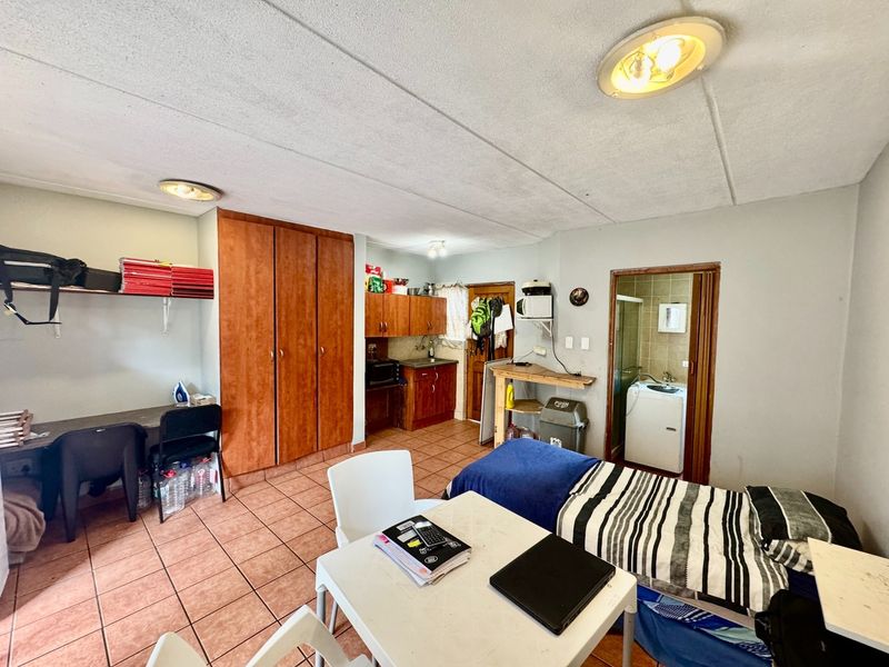 Open-plan studio apartment featuring tiled flooring, built-in kitchen cabinetry, and an integrated wardrobe, with an adjacent bathroom area.