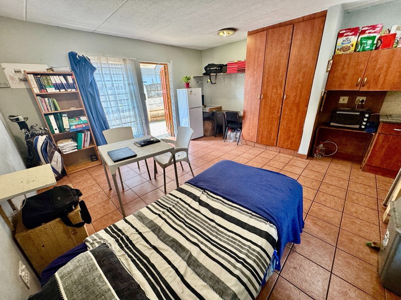 Open-plan studio apartment featuring tiled flooring, built-in wooden cupboards, and direct access to an outdoor area through a sliding door.