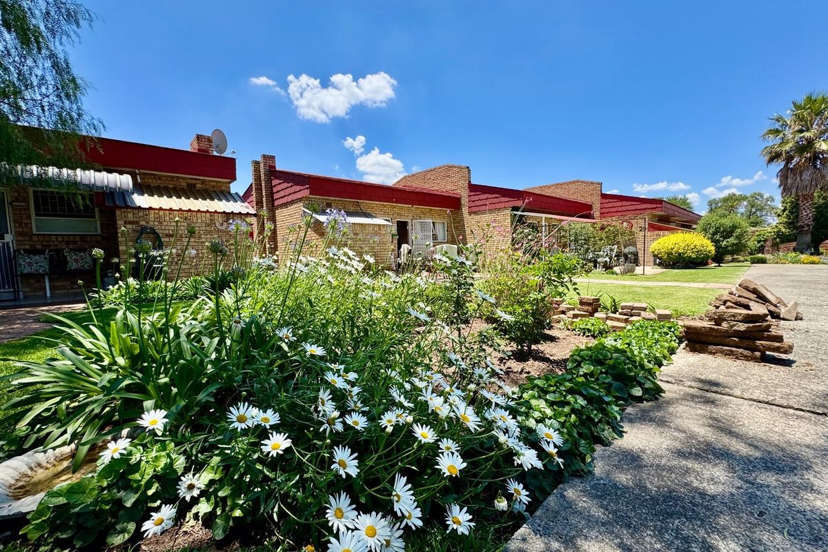 A view of the rear exterior of the apartment complex, featuring brick facades, metal roofing, and a well-maintained garden with a concrete pathway.
