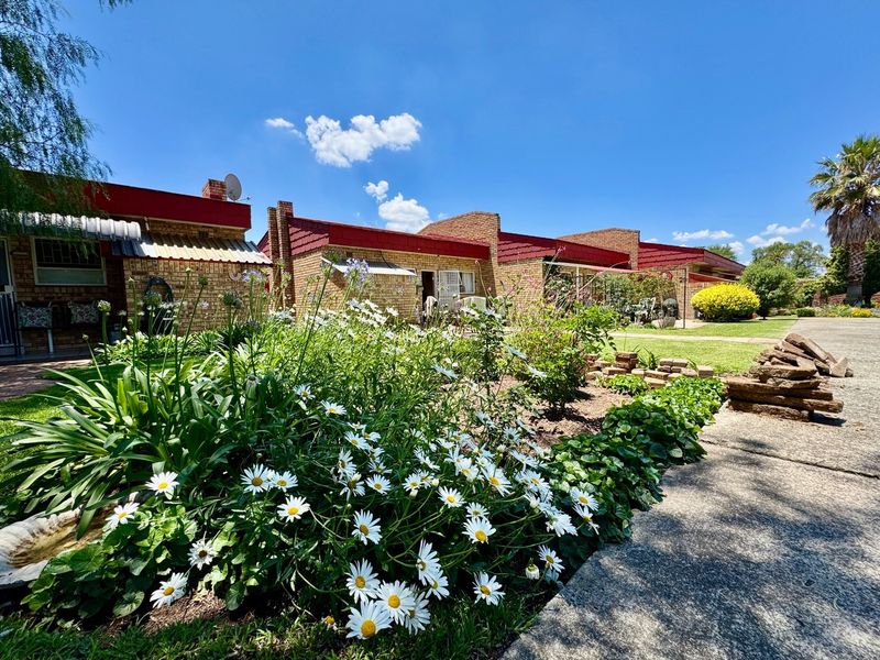 A view of the rear exterior of the apartment complex, featuring brick facades, metal roofing, and a well-maintained garden with a concrete pathway.