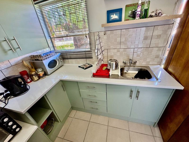Compact kitchen featuring light green cabinetry, white countertops, tiled backsplash, and a stainless steel sink with a window view.